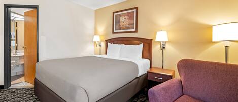 A hotel room with a large bed, two bedside lamps, a nightstand, a chair, and a door leading to a bathroom.