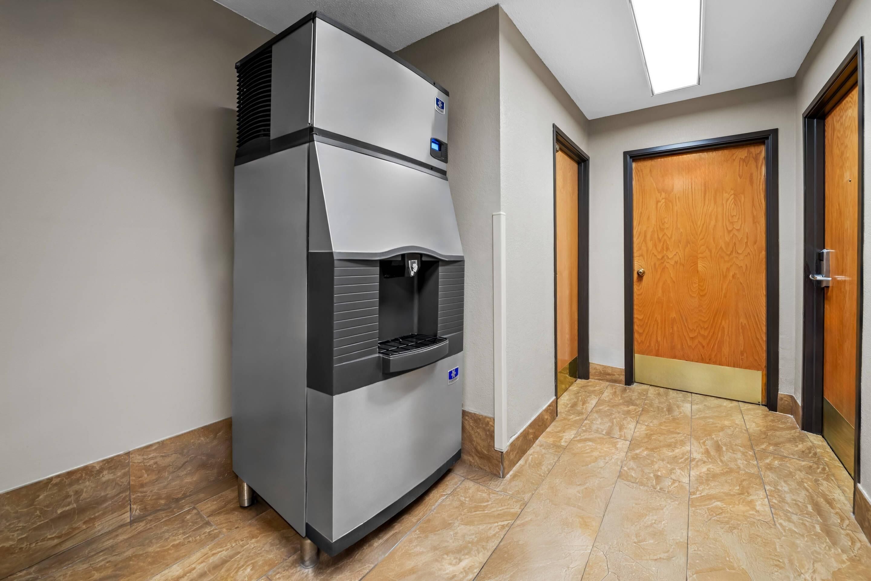A hallway with a commercial refrigerator, a wooden door, and a tiled floor.