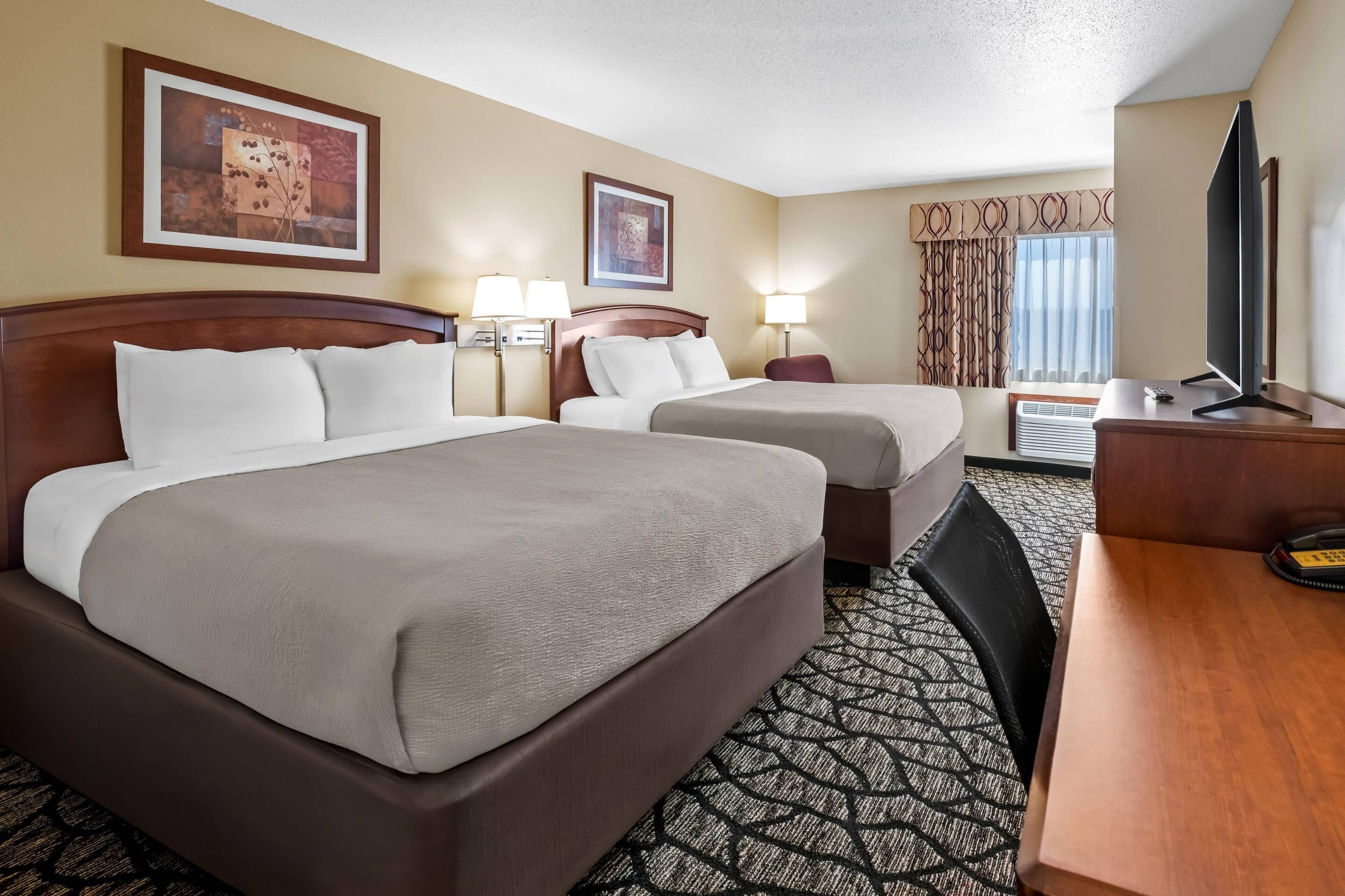 Une chambre d’hôtel avec deux lits, un bureau, une télévision et deux lampes.
