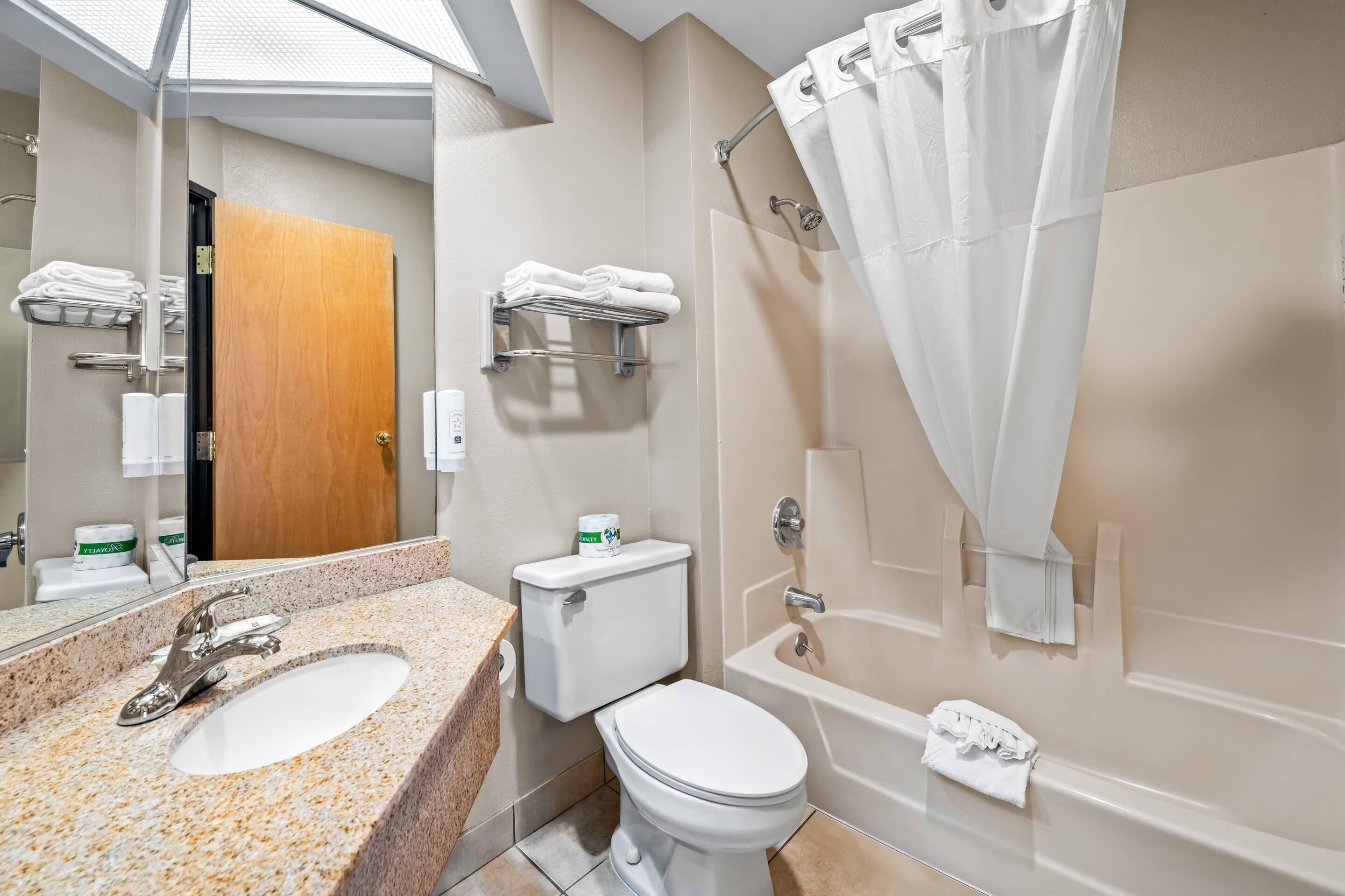 A modern bathroom with a granite countertop sink, a toilet, a bathtub, and a shower curtain.