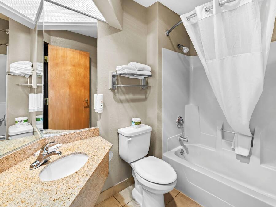 Un baño moderno con lavamanos de granito, inodoro, bañera y cortina de ducha.