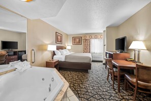 A hotel room with a large bed, a desk with a chair, a television, a desk lamp, a bathroom with a bathtub, and a patterned carpet. - Quality Inn La Crosse North (La Crosse)