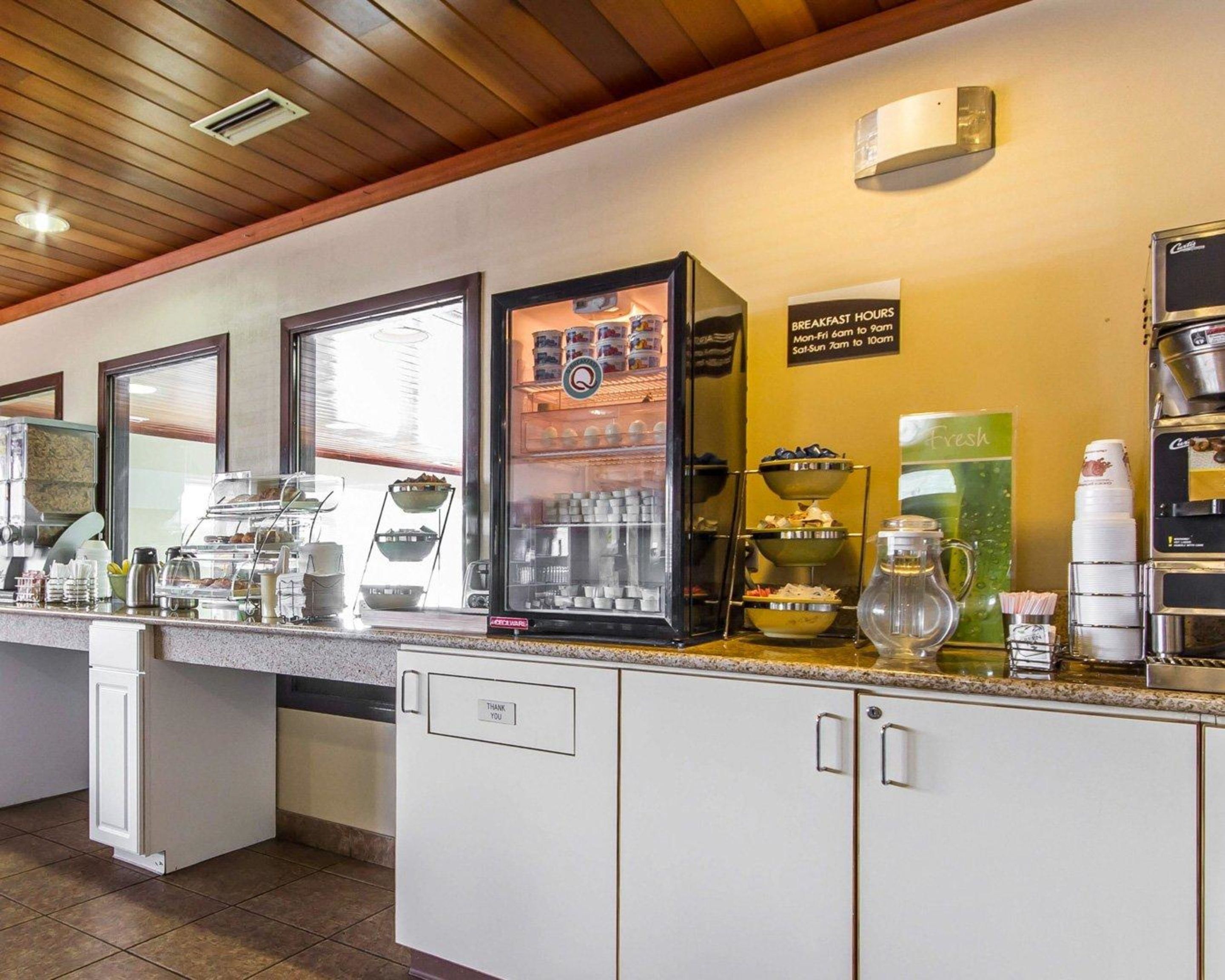 A breakfast station with self-service options, including a coffee machine, a fruit display, and a sign indicating breakfast hours.