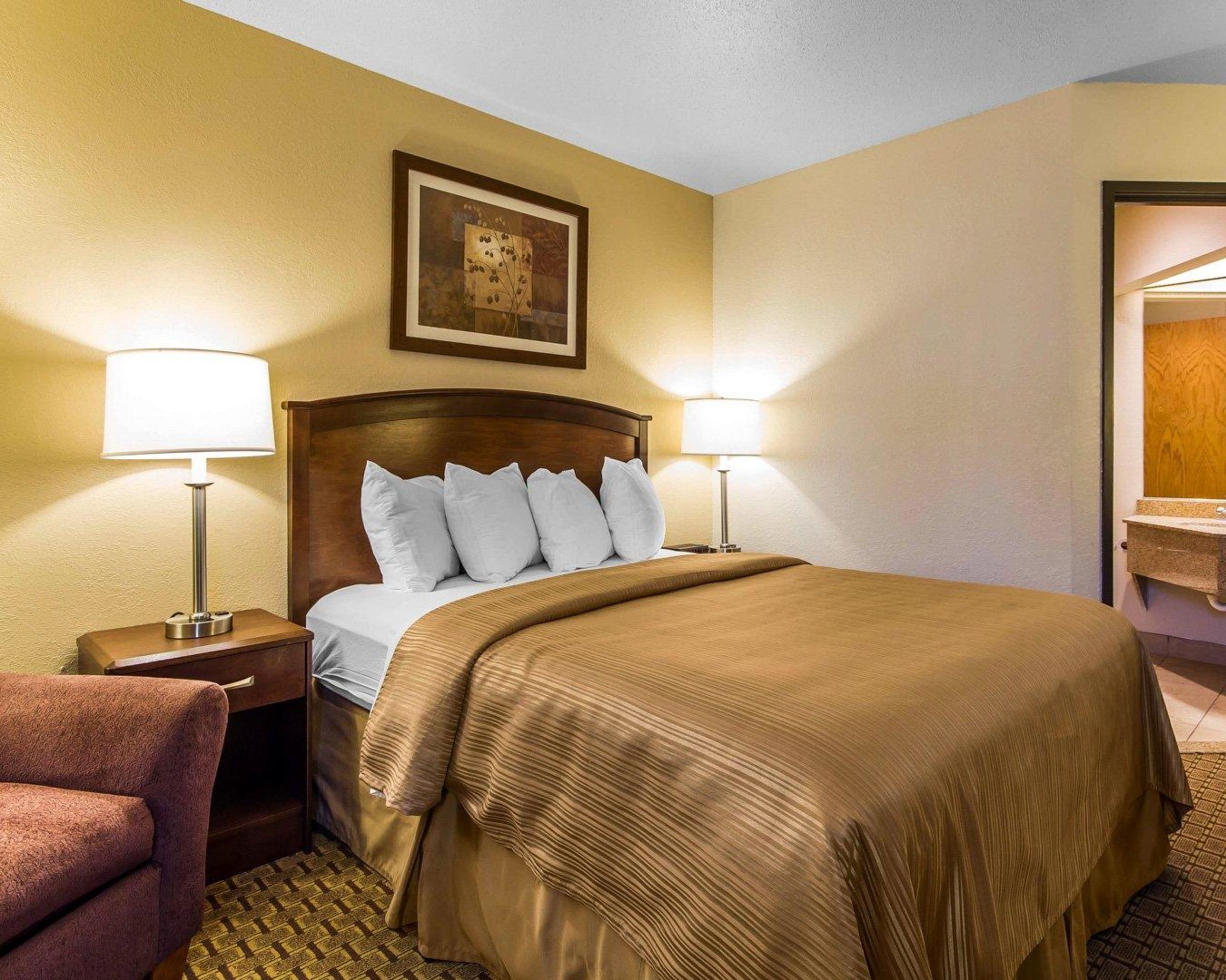 A hotel room with a bed, two bedside lamps, a framed picture on the wall, and a wooden nightstand.