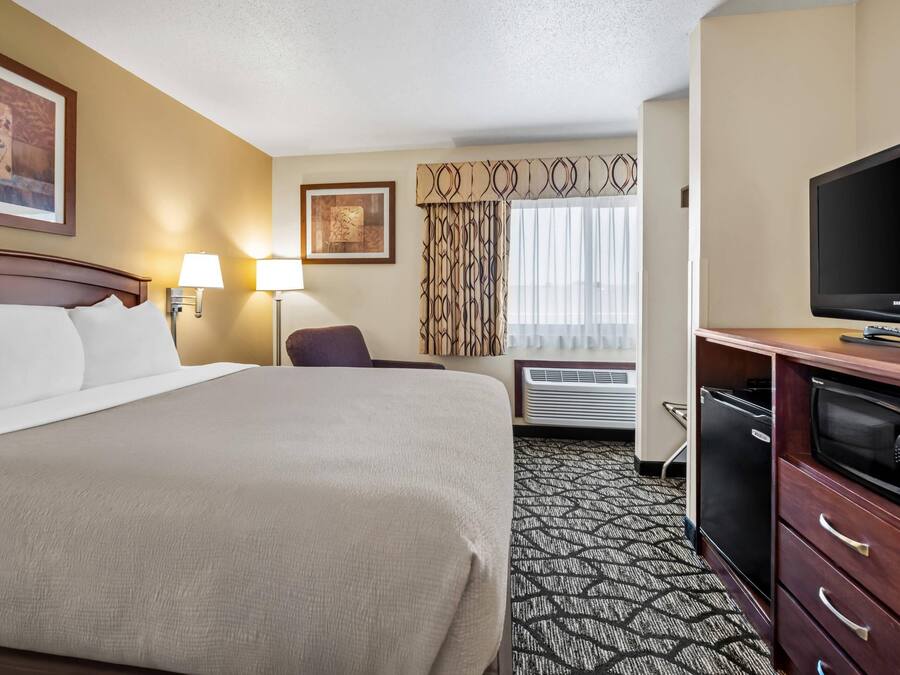 A hotel room with a large bed, a desk with a computer, a television, and a window with curtains.