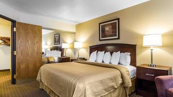 A hotel room with a large bed, two bedside tables with lamps, a wooden door, a mirror, and a framed picture on the wall.