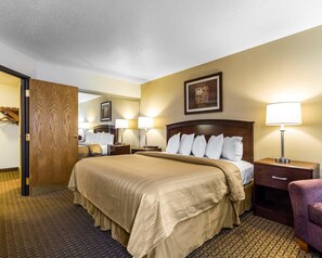 A hotel room with a large bed, two bedside tables with lamps, a wooden door, a mirror, and a framed picture on the wall.