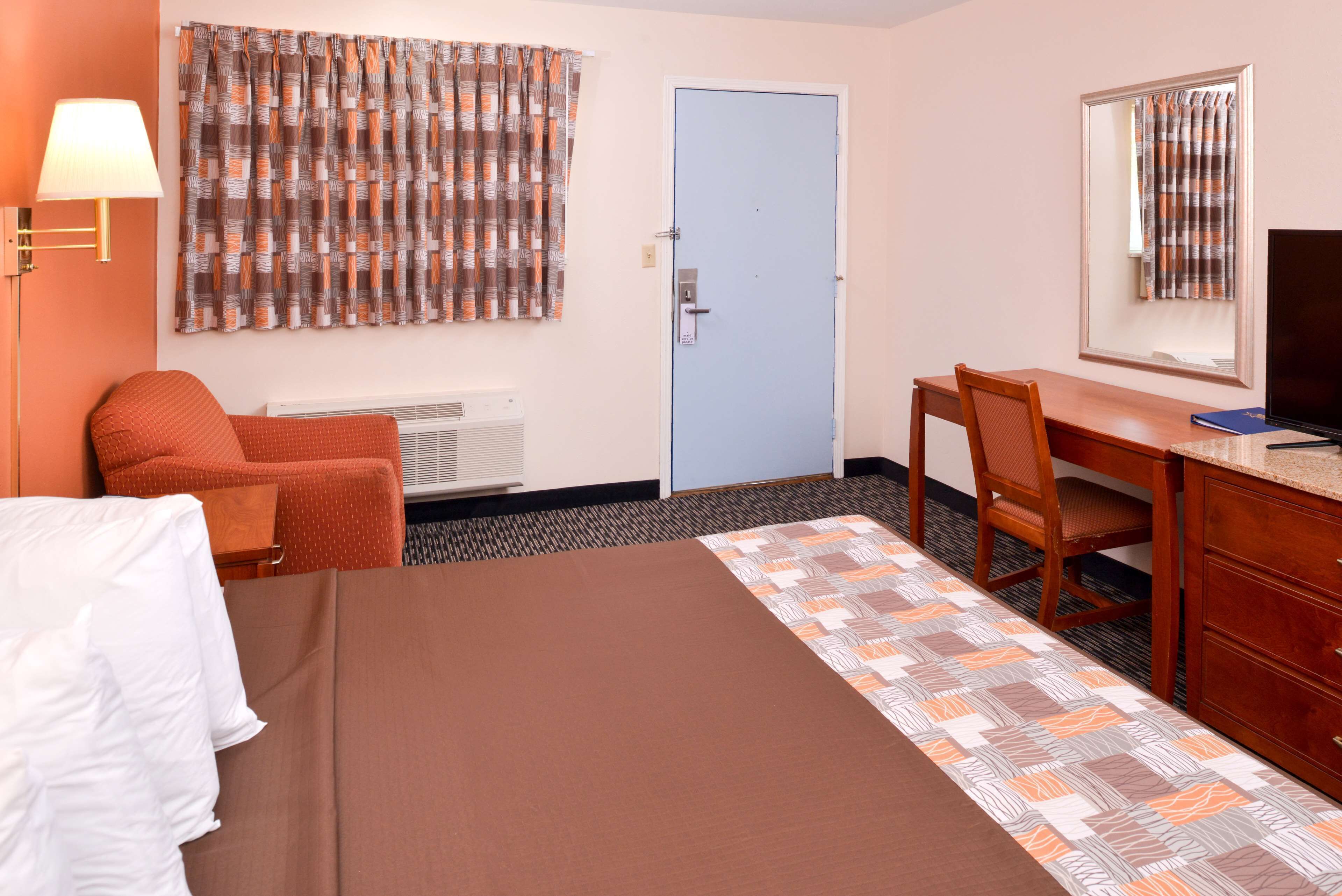 A hotel room with a bed, a desk, a chair, a lamp, a television, and a door.