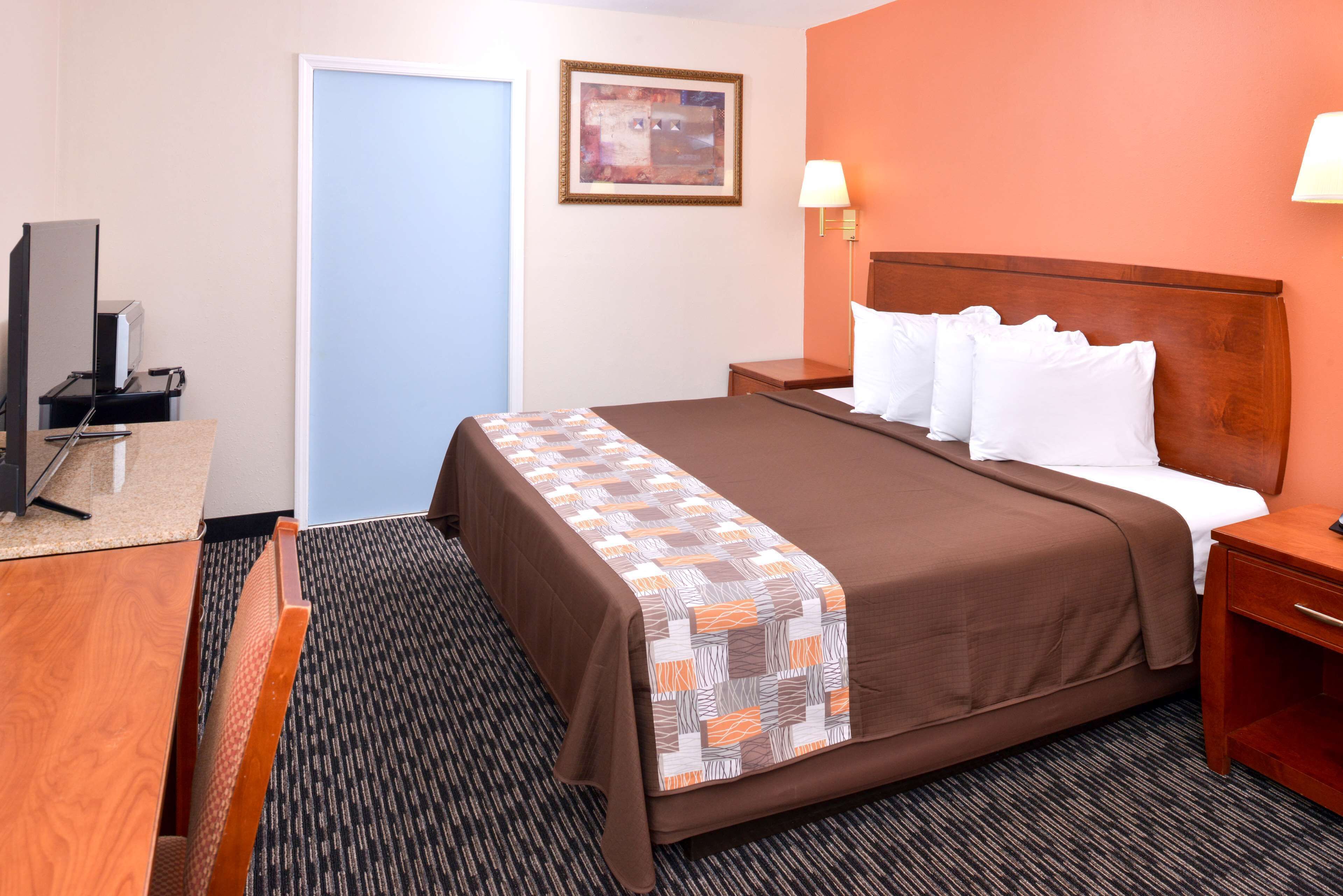 A hotel room with a bed, a desk, a chair, a television, and a door.