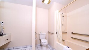 A bathroom with a toilet, a shower with grab bars, and a sink with a towel on the counter.