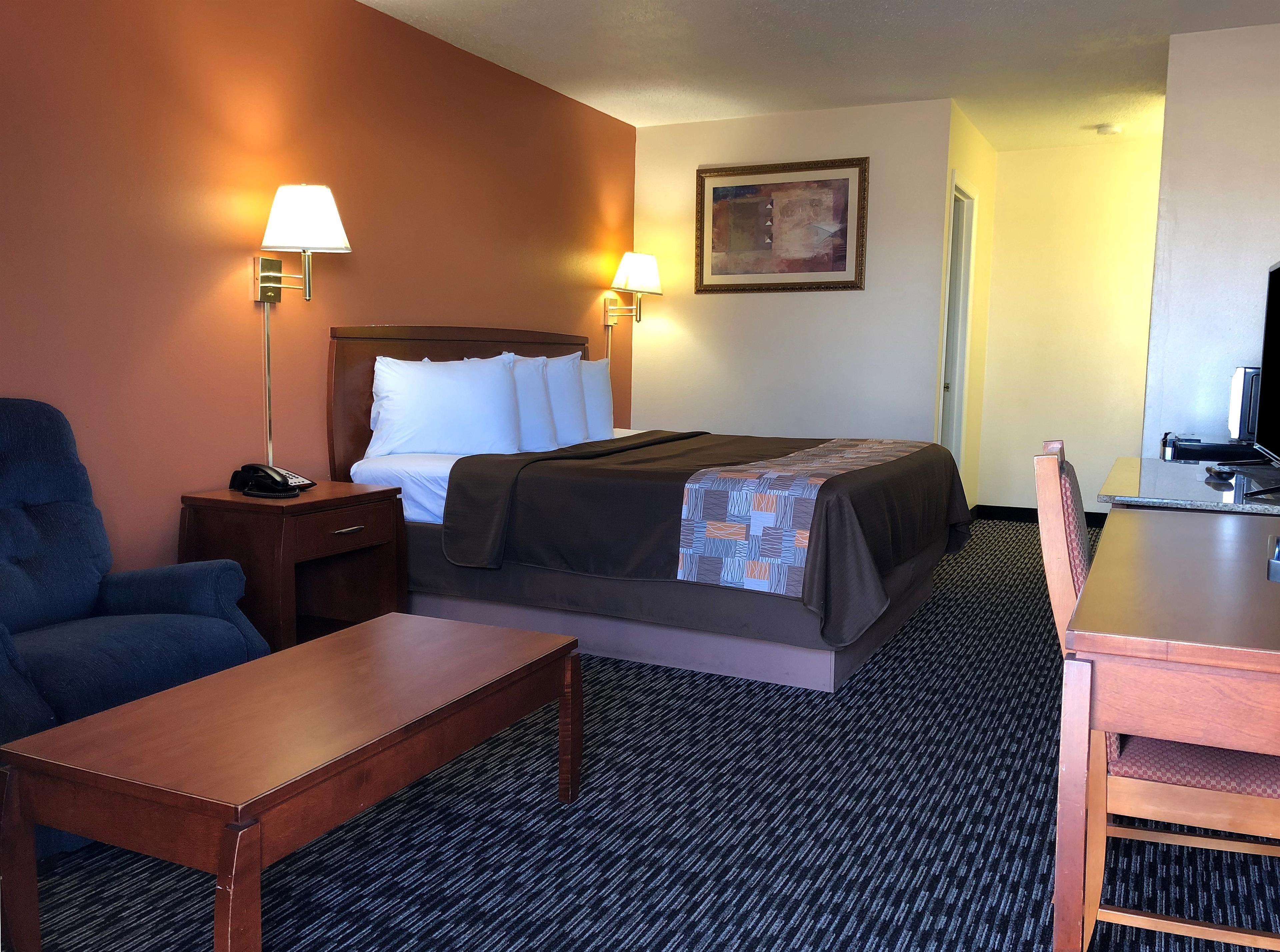 Una habitación de hotel con cama, lámparas de noche, escritorio, silla y una mesita.