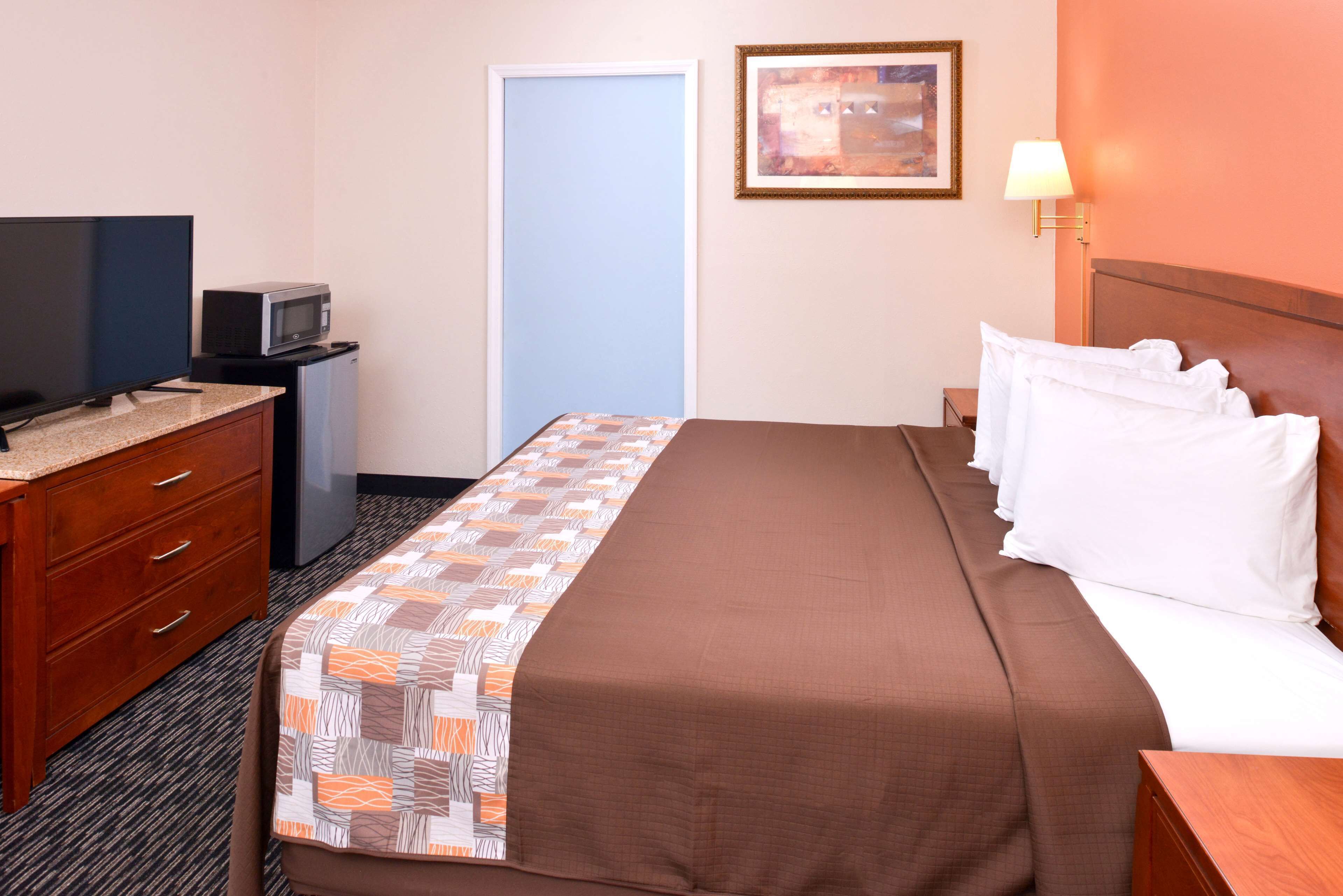 Una habitación de hotel con una cama, televisor, microondas, cómoda y una puerta.