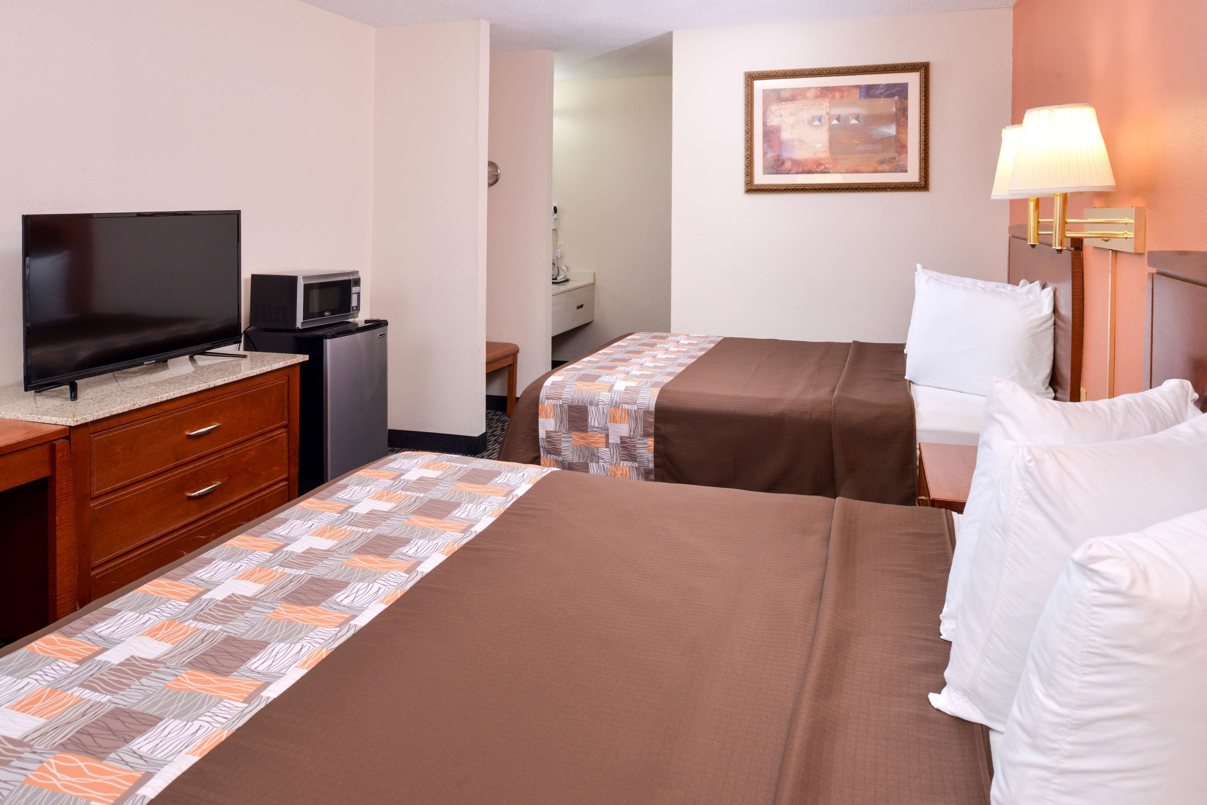 Une chambre d’hôtel avec deux lits, une télévision, un four à micro-ondes, un bureau avec des tiroirs et une lampe.