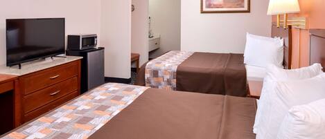 A hotel room with two beds, a television, a microwave, a desk with drawers, and a lamp.