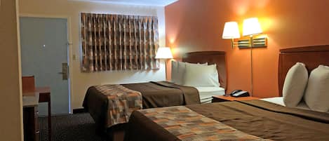 Habitación de hotel con dos camas, un escritorio y una silla. Hay dos lámparas en la pared y una puerta a la izquierda.