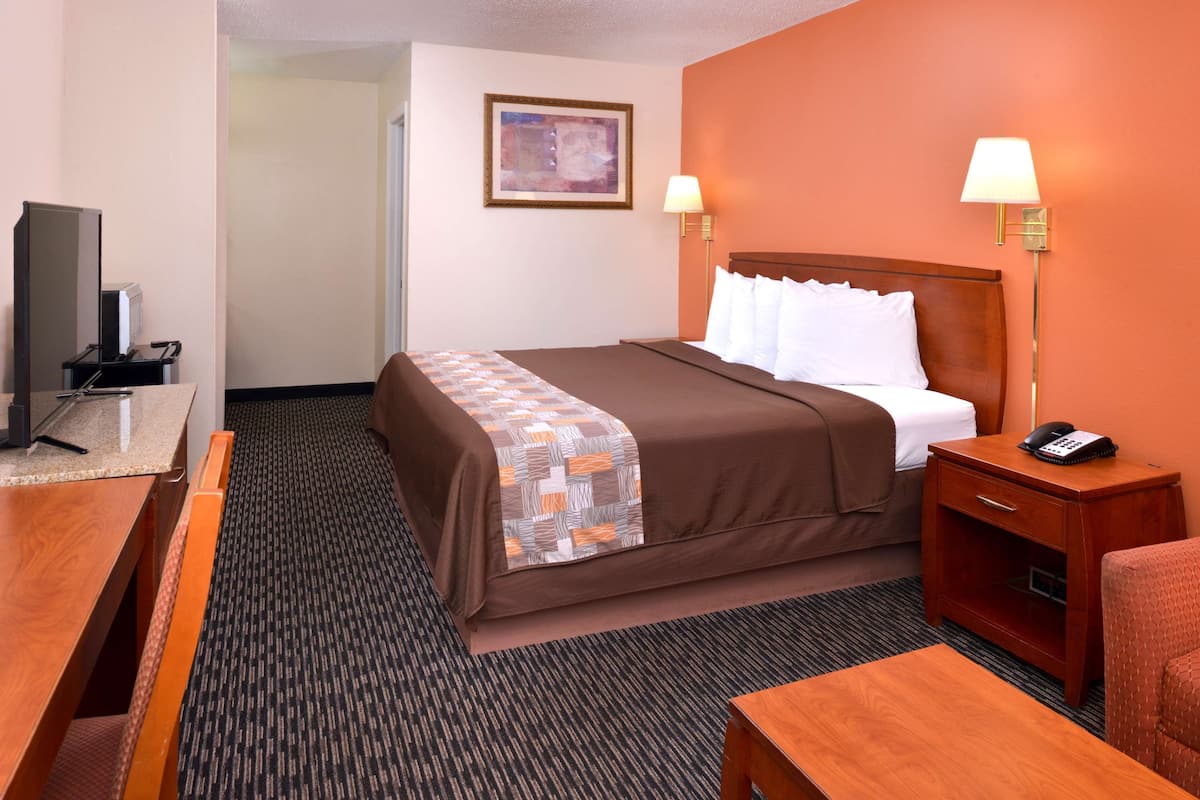 A hotel room with a bed, bedside table, lamp, and a television.