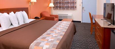 A hotel room with a large bed, a desk with a television, a chair, and a wall-mounted air conditioner.