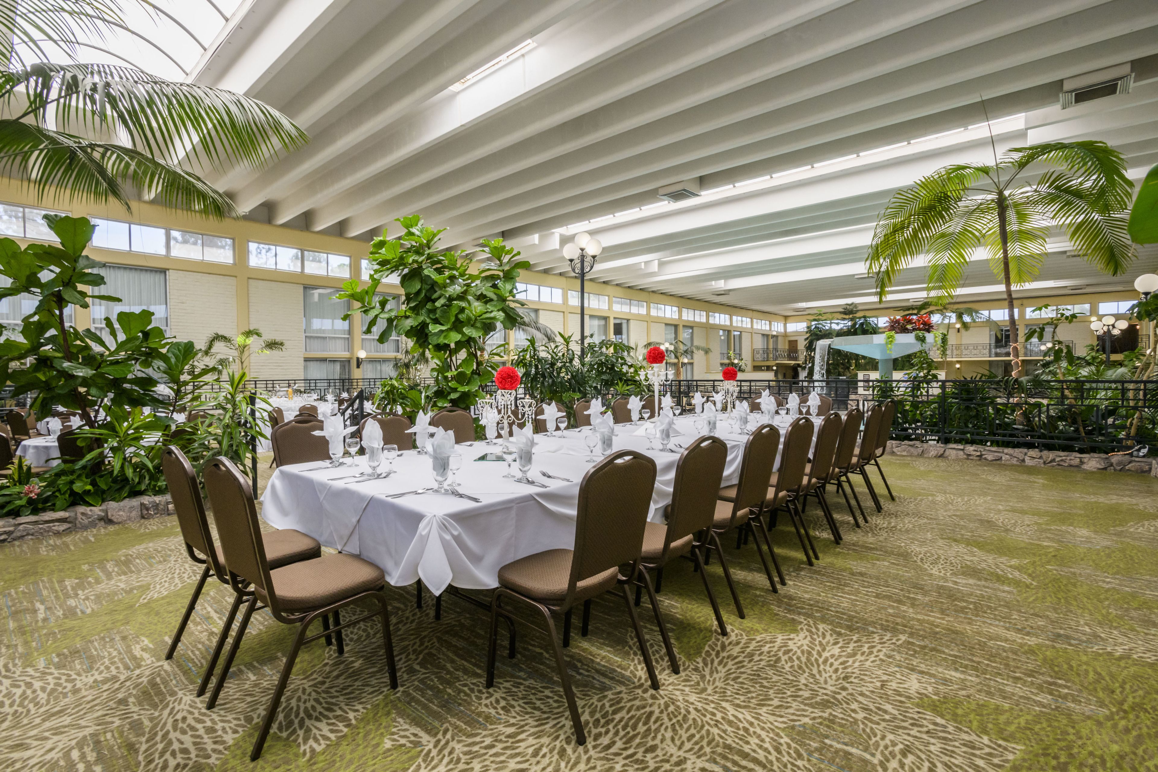 Una larga mesa dispuesta para un evento formal en un amplio espacio interior con techos altos y ventanas grandes.