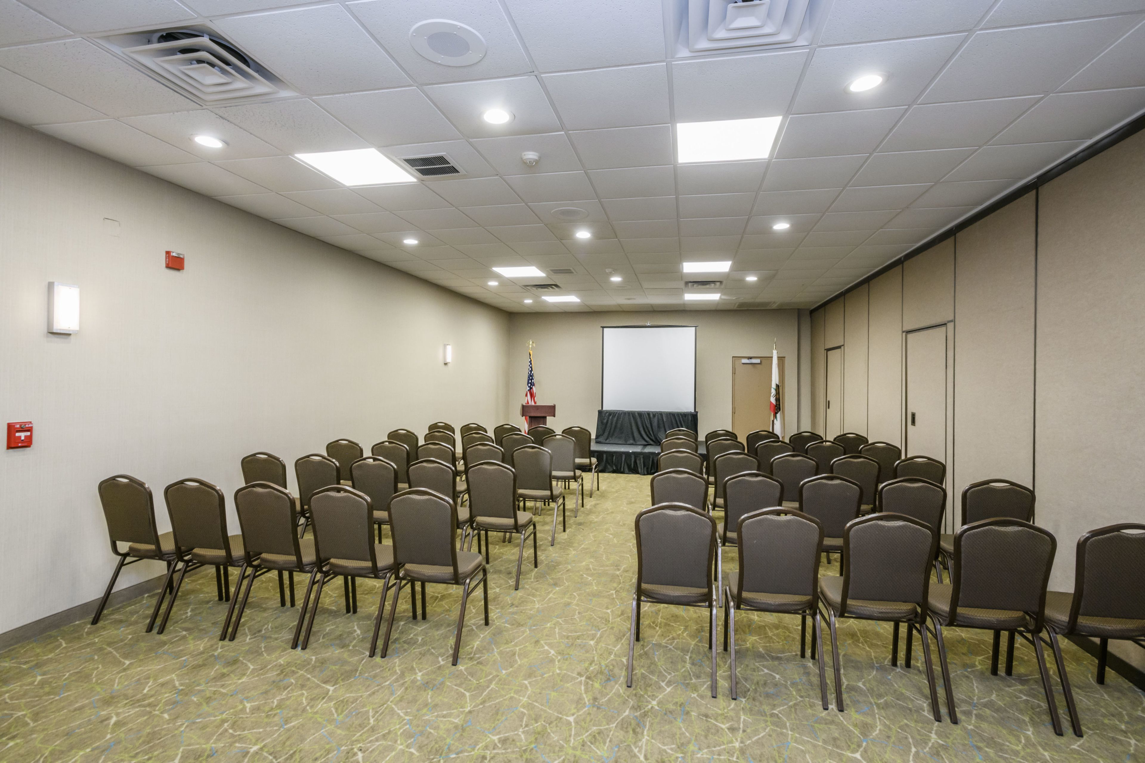 A conference room with rows of chairs, a podium, a projector screen, and a flag.