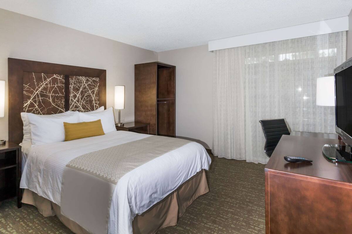Une chambre d’hôtel avec un grand lit, un bureau avec un ordinateur, une chaise et une armoire.