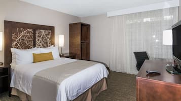 A hotel room with a large bed, a desk with a computer, a chair, and a wardrobe.