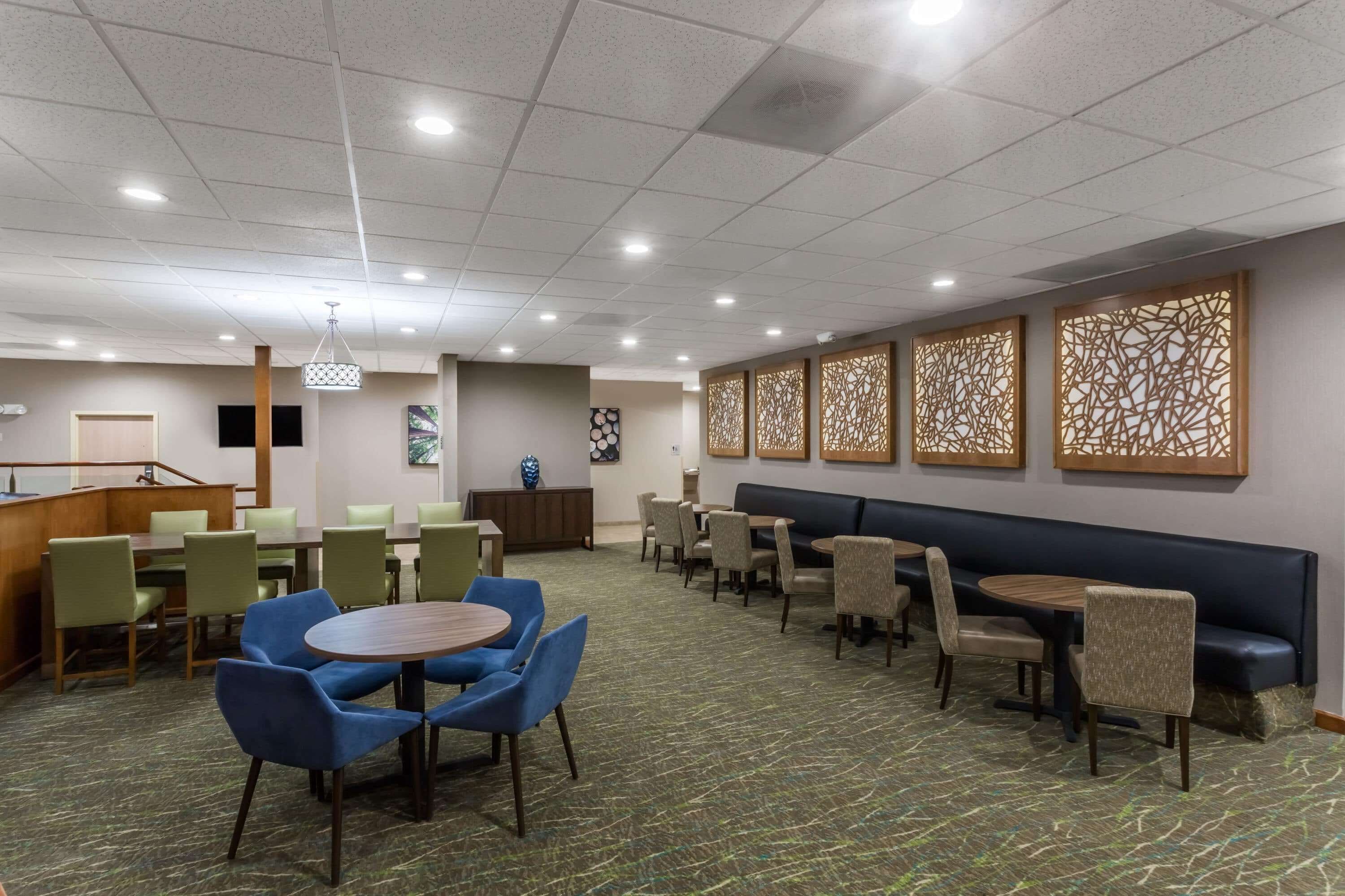 A hotel lobby with multiple seating areas, including round tables and booths, a reception desk, and decorative wall panels.
