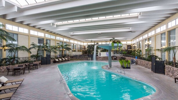 An indoor swimming pool with a waterfall feature, surrounded by lounge chairs and potted plants. - Wyndham Garden Fresno Yosemite Airport (Fresno)
