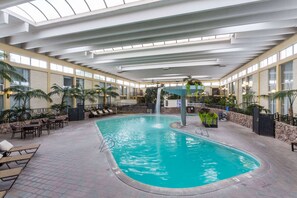 Indendørs swimmingpool med et vandfald, omgivet af liggestole og plantekasser.