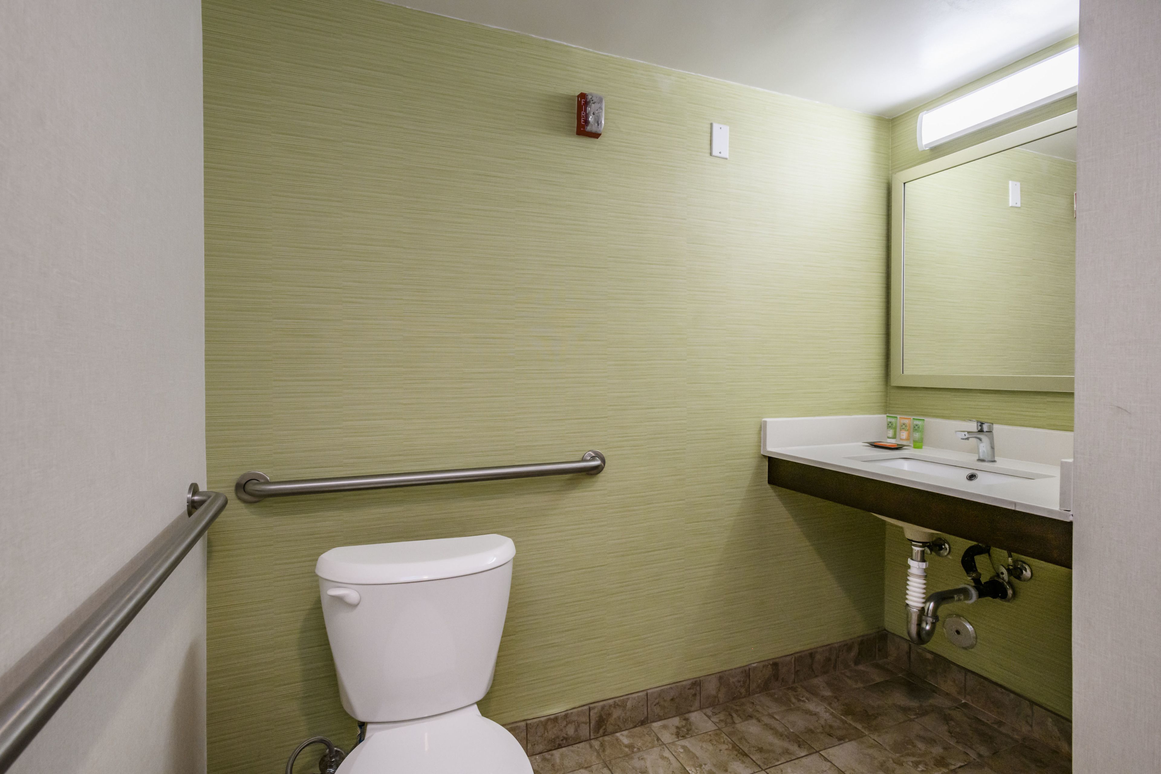 A bathroom with a toilet, a handrail, a sink, and a mirror.