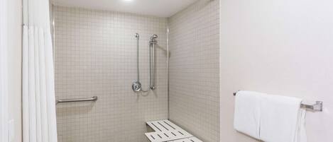 Un espacio de ducha pequeño con azulejos, una barra de apoyo, un cabezal de ducha y un perchero para toallas.