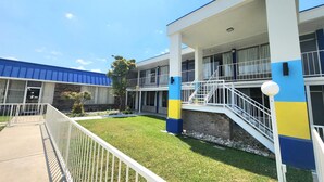 A building with a blue roof, white and blue exterior walls, a covered outdoor area with a staircase, and a fenced yard. - Days Inn by Wyndham Seguin TX (Seguin)