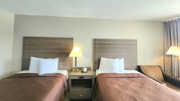 Une chambre d’hôtel avec deux lits, chacun recouvert d’une couverture marron et agrémenté d’oreillers blancs. Une table de chevet se trouve entre les deux lits, avec une lampe et un téléphone.