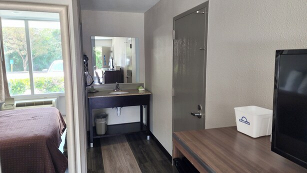 A hotel room with a bed, a bathroom with a sink and mirror, a door, and a small white box. - Days Inn by Wyndham Seguin TX (Seguin)