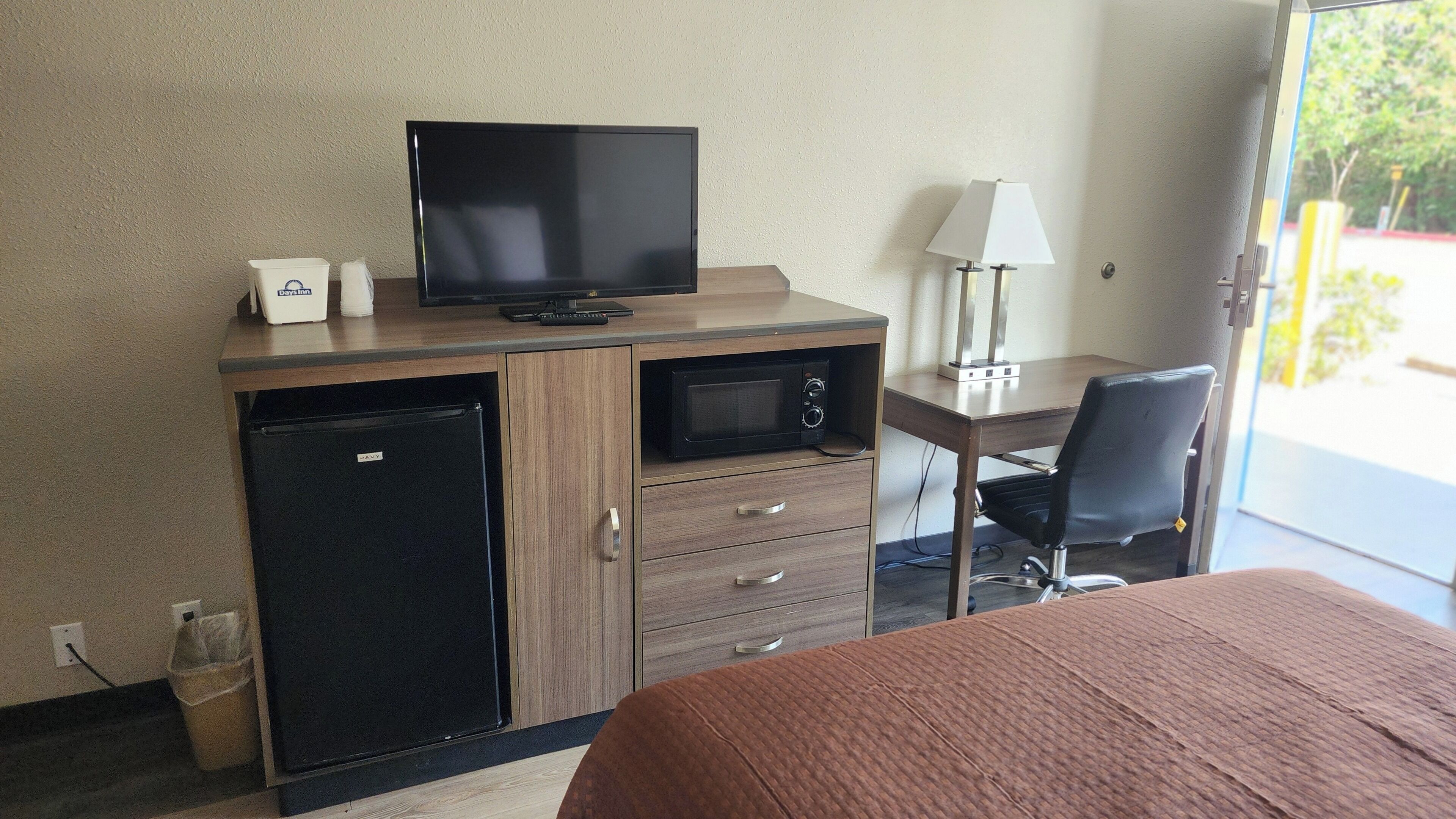 A hotel room with a bed, a desk with a computer, a microwave, a TV, and a lamp.