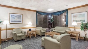 A hotel room with a seating area featuring two sofas, two armchairs, and a coffee table. There are two lamps, a potted plant, and a window with curtains. - Days Inn by Wyndham Seguin TX (Seguin)