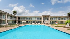 A swimming pool with lounge chairs and umbrellas, surrounded by a multi-story building with balconies. - Days Inn by Wyndham Seguin TX (Seguin)