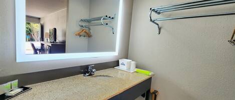 A modern bathroom with a granite countertop, a large mirror, a towel rack, and a sink with a faucet.
