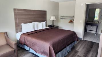 A hotel room with a large bed, a nightstand, a lamp, a chair, and a bathroom visible through an open door.