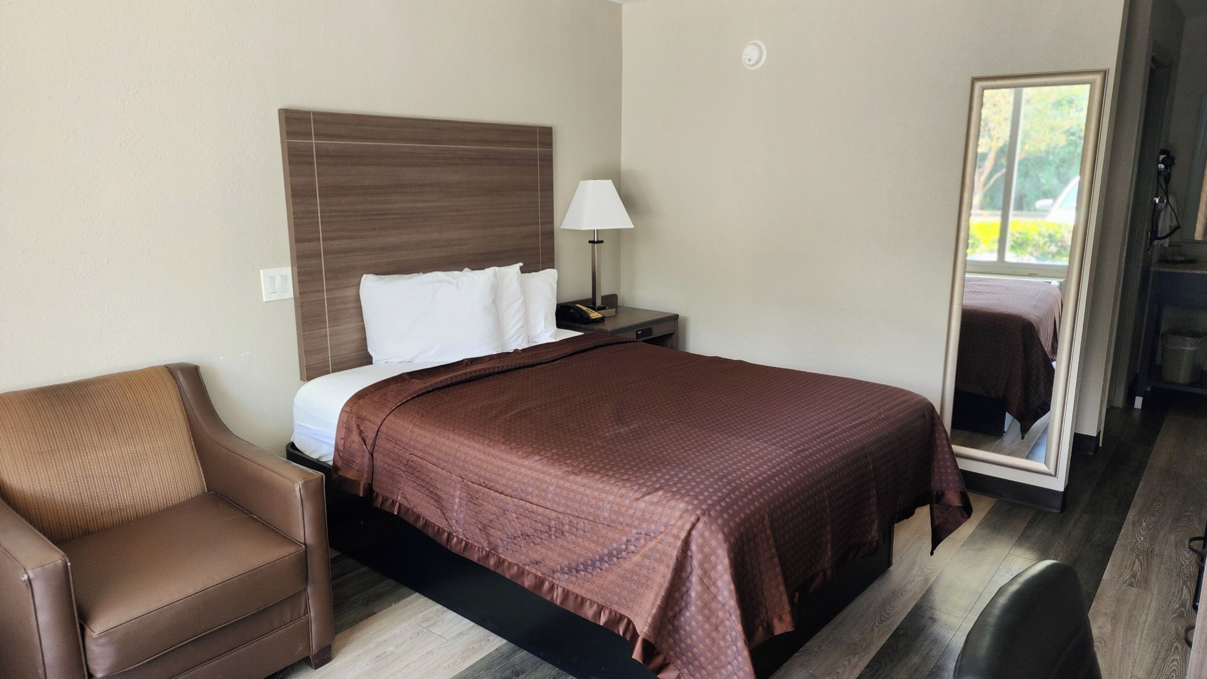 A hotel room with a bed, a nightstand, a lamp, a chair, and a mirror.