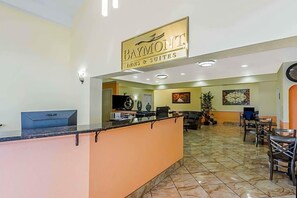 A reception area with a sign for Baymont Inn & Suites, a reception desk, a computer, and a seating area with chairs and tables. - Baymont by Wyndham San Antonio Near South Texas Medical Ctr (San Antonio)