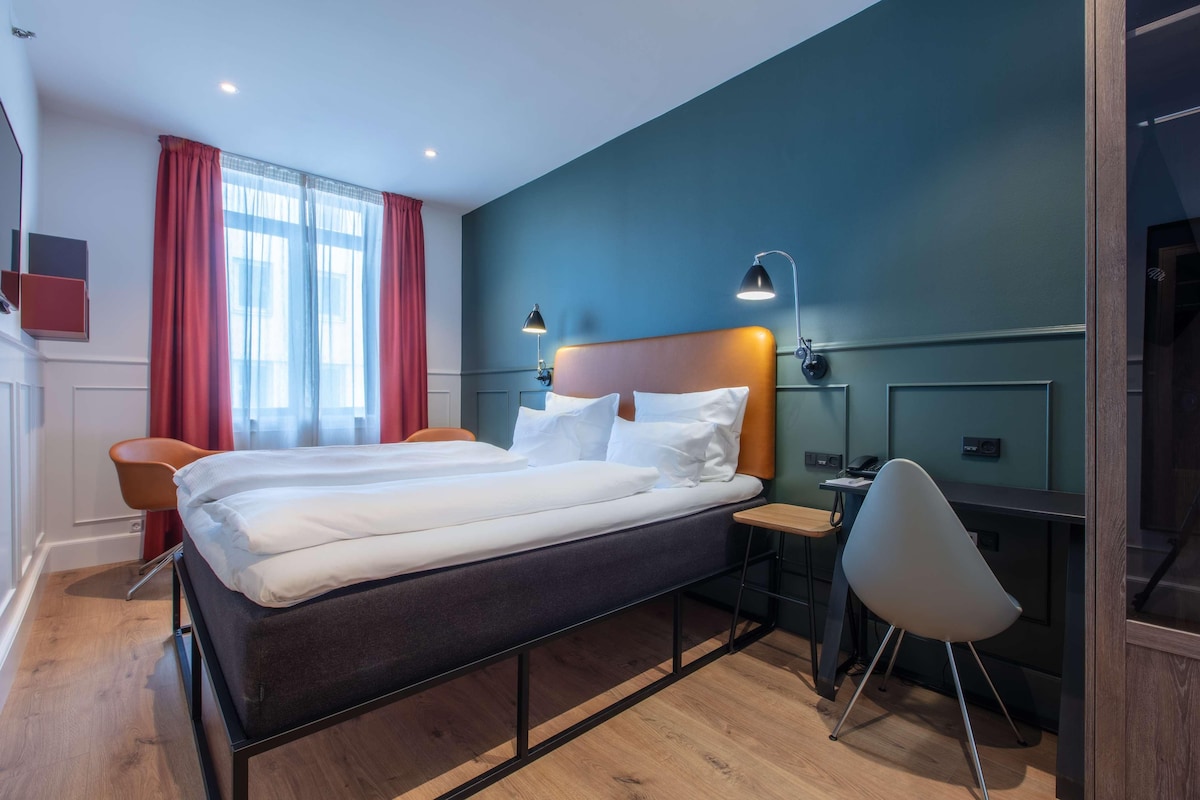 Una habitación de hotel moderna con una cama grande, dos mesitas de noche, un escritorio y una silla.