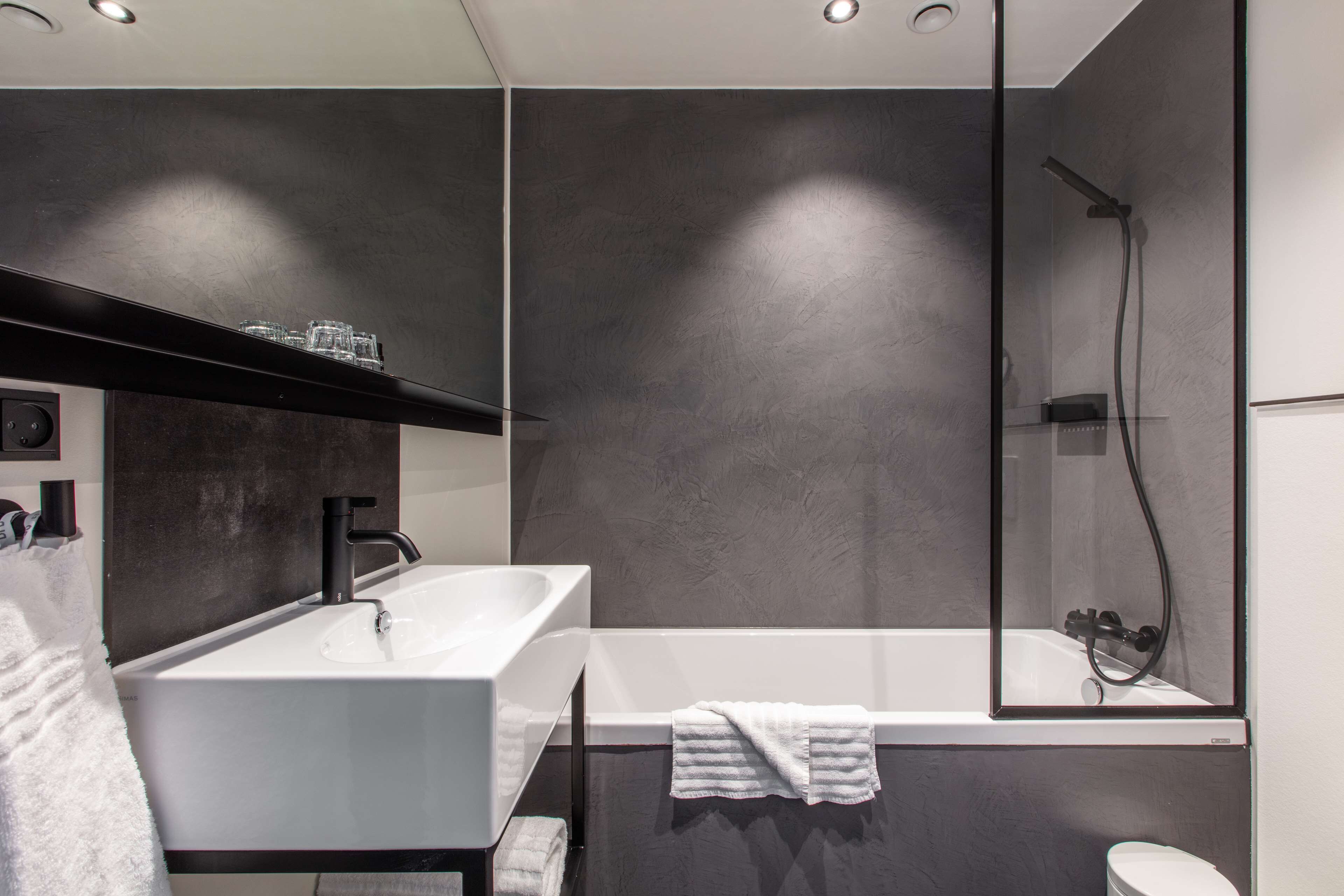 Un baño moderno con lavamanos blanco, un espejo grande y zona de ducha.