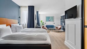 A modern hotel room with a large bed, a TV, a desk, and a seating area with chairs.