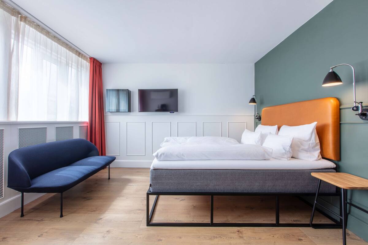 A hotel room with a bed, a blue sofa, a TV, and a lamp.