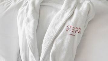 Una bata blanca con el bordado 'GRAND HYATT', colocada sobre una cama con almohadones blancos.