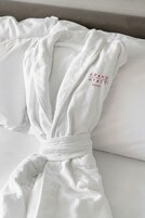 Una bata blanca con el bordado 'GRAND HYATT', colocada sobre una cama con almohadones blancos.