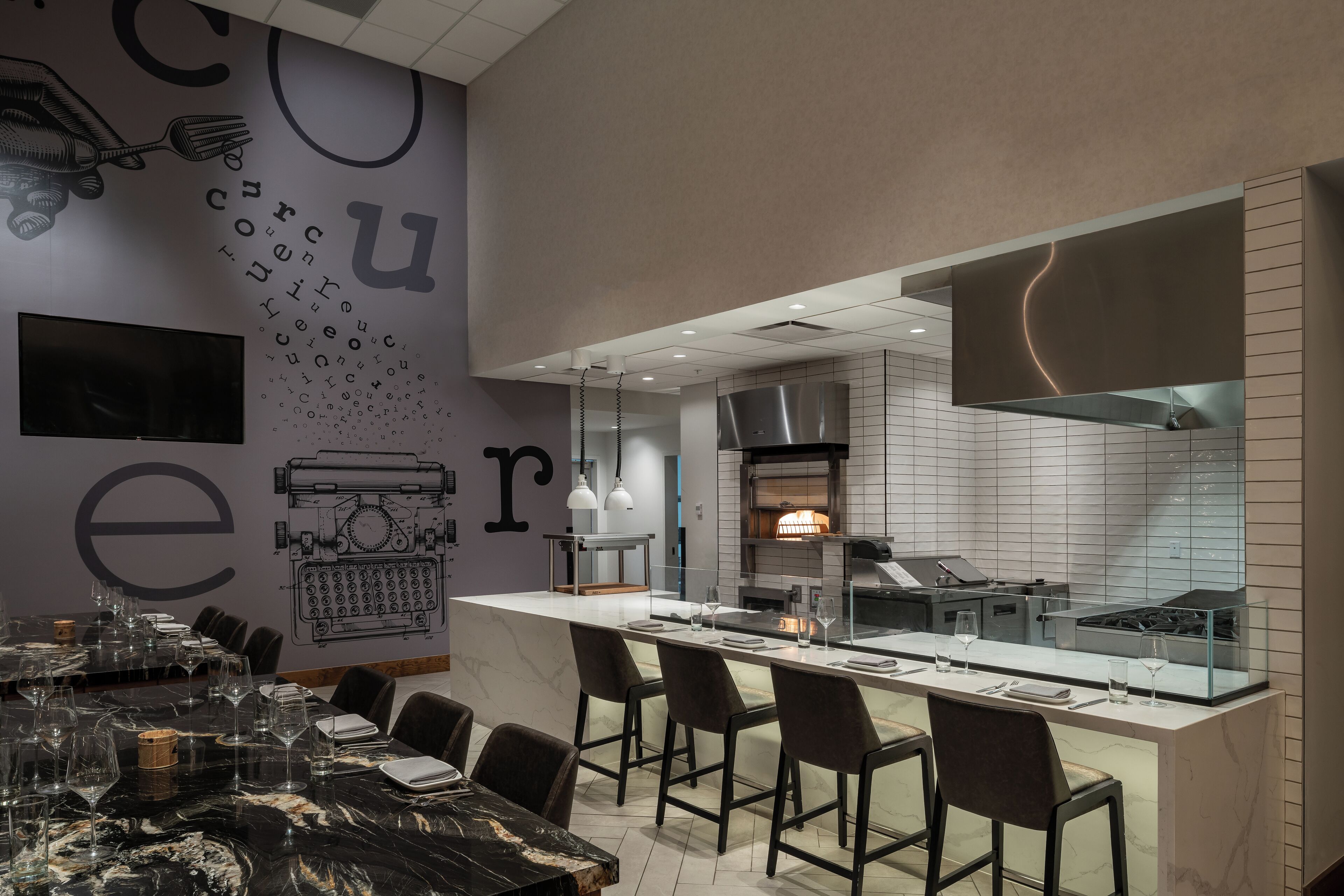A modern restaurant with a bar area, marble flooring, and a kitchen visible through a glass partition.