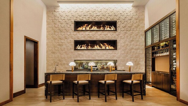 A bar area with a brick wall, bar stools, and a shelf with glasses.