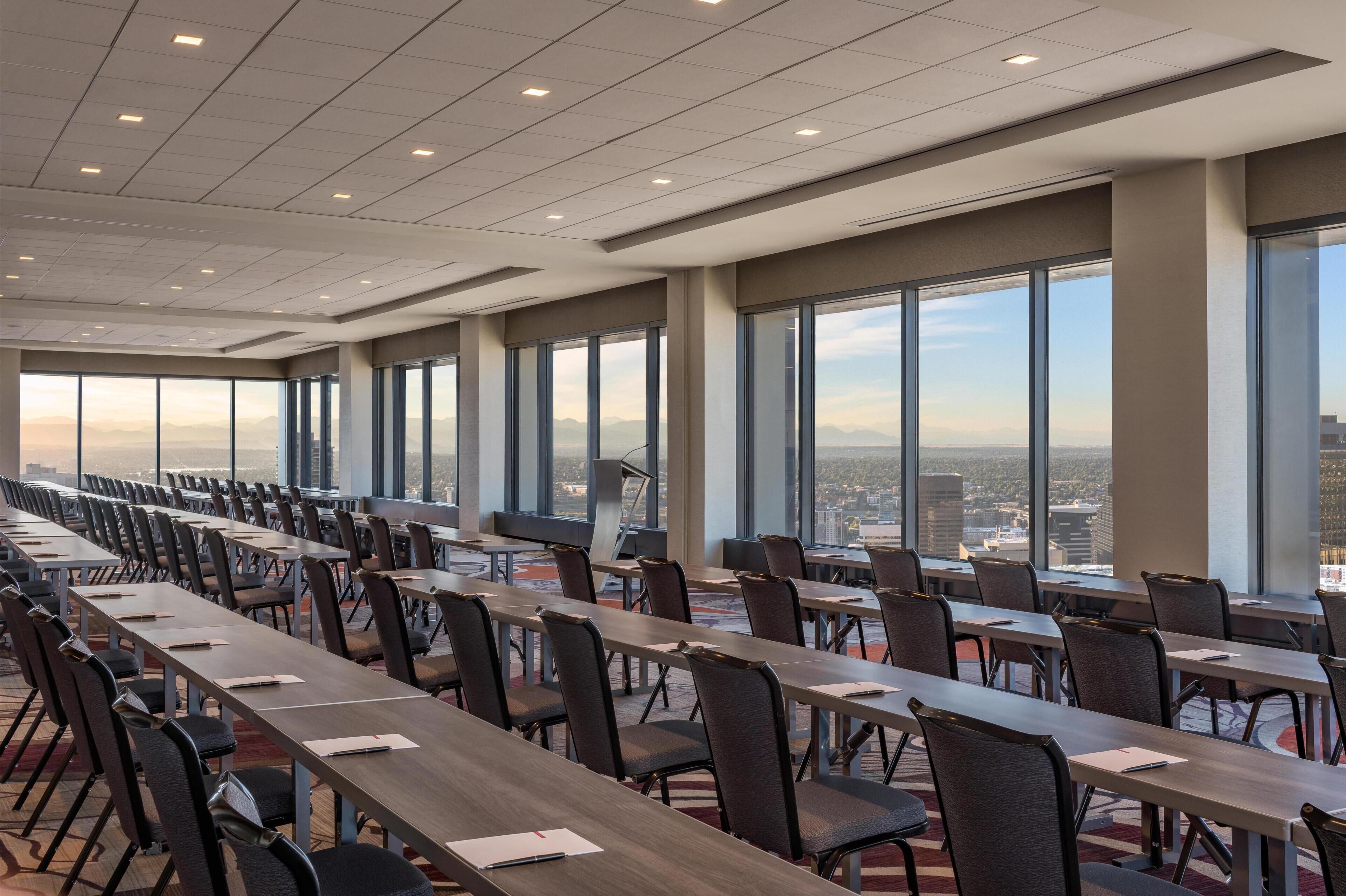 A conference room with long tables and chairs, large windows with a city view, and a modern ceiling design.