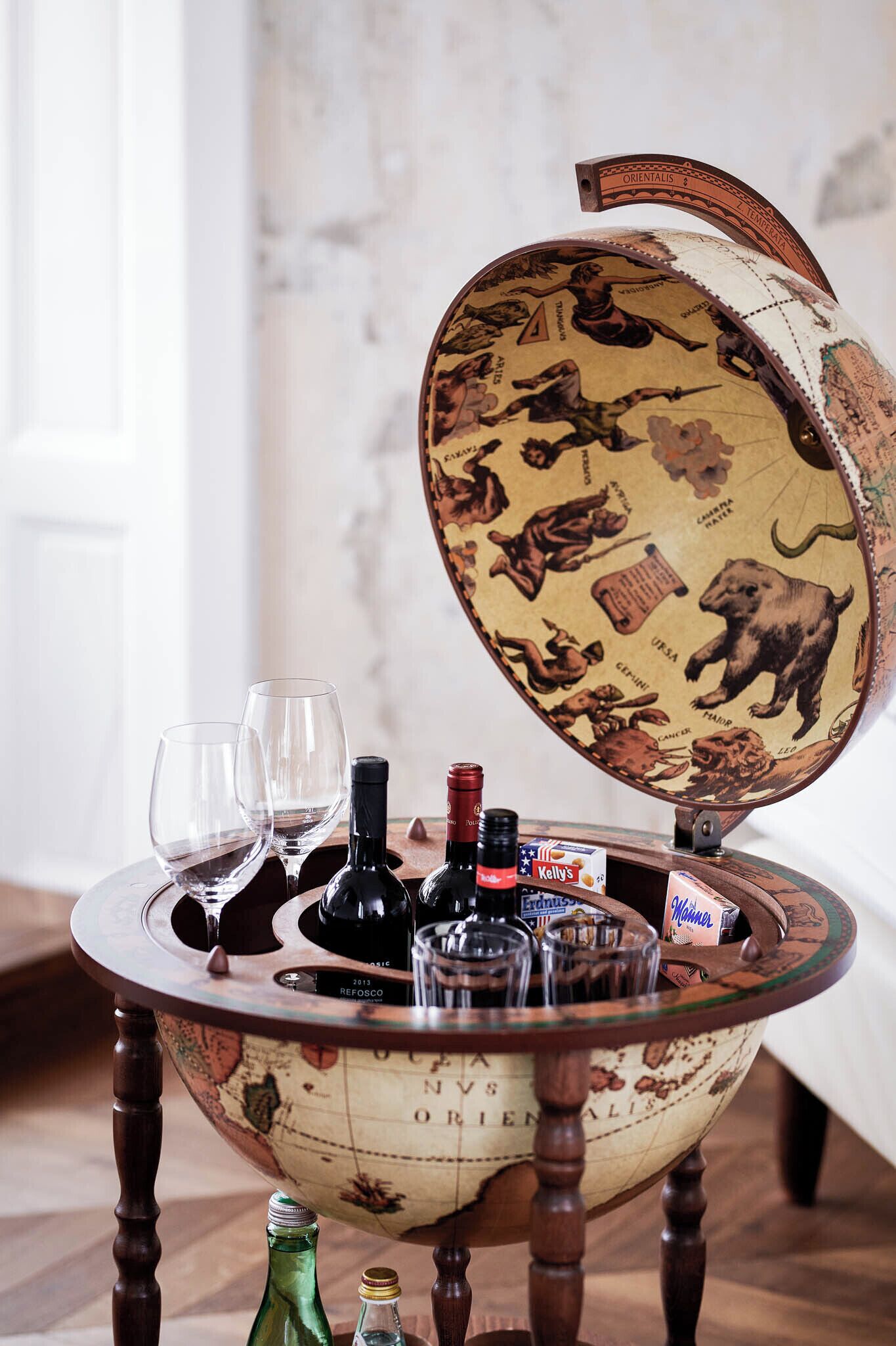 Uma mesa globo com design de mapa mundi, rodeada por garrafas de vinho e copos.